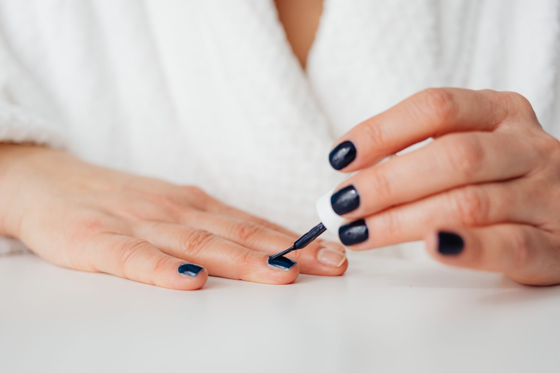 A woman applying dark nail polish at home, showcasing beauty and self-care.